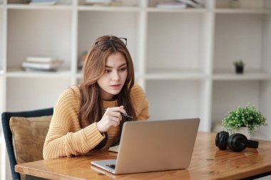 Güzel beyaz bir kız öğrenci üniversitede uzaktan öğrenim görüyor. Evde dizüstü bilgisayar ve not defteriyle bir masada oturuyor ve bir video konferans dersi izliyor. Yüksek kalite