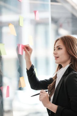 Güzel bayan çalışanlar renkli yapışkan notlar yönetici listesine yazarlar, konsantre çift ırklı kadınlar başlangıç beyin fırtınası planı üzerinde çalışırlar cam duvardaki çıkartmalar üzerinde işbirliği yaparlar. Yüksek kalite fotoğraf