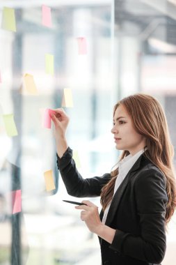 Güzel bayan çalışanlar renkli yapışkan notlar yönetici listesine yazarlar, konsantre çift ırklı kadınlar başlangıç beyin fırtınası planı üzerinde çalışırlar cam duvardaki çıkartmalar üzerinde işbirliği yaparlar. Yüksek kalite fotoğraf