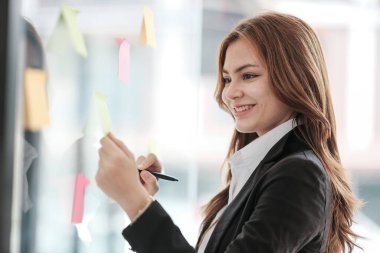 Güzel bayan çalışanlar renkli yapışkan notlar yönetici listesine yazarlar, konsantre çift ırklı kadınlar başlangıç beyin fırtınası planı üzerinde çalışırlar cam duvardaki çıkartmalar üzerinde işbirliği yaparlar. Yüksek kalite fotoğraf
