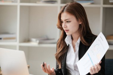 Dizüstü bilgisayarla video konferansı yapan güzel bir kadın iş geliştirme grafiği sunuyor ve ofisteki meslektaşıyla tartışıyor. Yüksek kalite fotoğraf