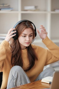 Güzel beyaz bir kız öğrenci üniversitede uzaktan öğrenim görüyor. Evde dizüstü bilgisayar ve not defteriyle bir masada oturuyor ve bir video konferans dersi izliyor. Yüksek kalite