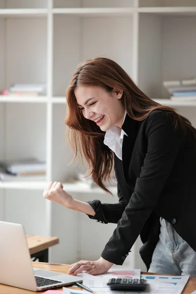 stock image Portrait of Beautiful happy young business woman celebrating success with arms up in front of laptop. Freelancer finished project. High quality photo.