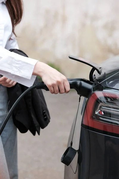 stock image Young woman traveling by electric car having stop at charging station standing plugging charger close-up. High quality photo