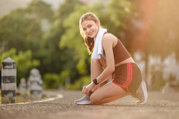 Kadın koşucu diz çöküp ayakkabı bağını sokakta bağlıyor. Spor ayakkabısı bağlayan kadın. Gün batımı ve güneş ışığıyla parkta ayakkabı bağı bağlayan genç bir kadın. Yüksek kalite fotoğraf