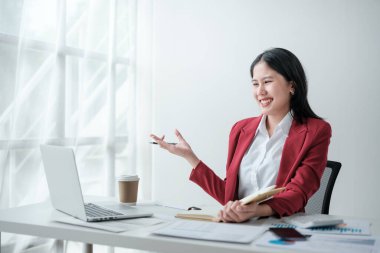 Gülümseme portresi kırmızı takım elbiseli Asyalı güzel bir iş kadını ofis bilgisayarında çalışıyor. Küçük işletme... yüksek kaliteli fotoğraf.