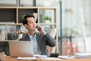Mutlu Asyalı iş adamı ofisteki akıllı telefonlar, tabletler ve dizüstü bilgisayarlarla konuşma zevkine sahip. Yüksek kaliteli fotoğraf.
