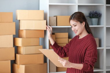 Girişim KOBİ küçük işletme girişimcisi önlük giyen Asyalı kadın dizüstü bilgisayar ve kutu kullanarak çevrimiçi müşterilere, çevrimiçi sme iş fikirlerine satış hazırlamak için siparişleri alır ve gözden geçirir