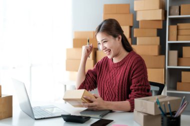 Girişim KOBİ küçük işletme girişimcisi önlük giyen Asyalı kadın dizüstü bilgisayar ve kutu kullanarak çevrimiçi müşterilere, çevrimiçi sme iş fikirlerine satış hazırlamak için siparişleri alır ve gözden geçirir