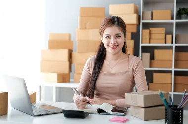 Girişim KOBİ küçük işletme girişimcisi önlük giyen Asyalı kadın dizüstü bilgisayar ve kutu kullanarak çevrimiçi müşterilere, çevrimiçi sme iş fikirlerine satış hazırlamak için siparişleri alır ve gözden geçirir