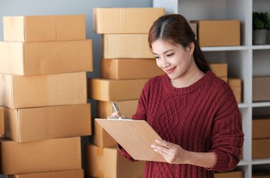 Girişim KOBİ küçük işletme girişimcisi önlük giyen Asyalı kadın dizüstü bilgisayar ve kutu kullanarak çevrimiçi müşterilere, çevrimiçi sme iş fikirlerine satış hazırlamak için siparişleri alır ve gözden geçirir