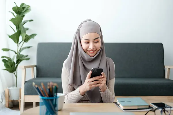 Young business Asian Business Muslim woman in hijab using a Phone, Sitting near the window in the living room. High quality photo