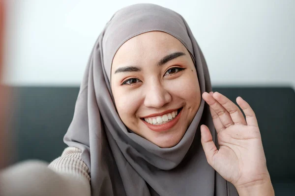 A beautiful asian woman in hijab talks on video call, online meeting with colleagues and clients, woman cheerfully waves her hand and greets interlocutors online. High quality photo