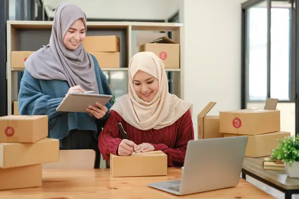 Friend muslim female two work business sme online shopping working on laptop computer with parcel box on desk at home, SME online business and delivery concept. High quality photo