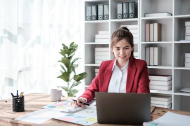 Güzel Asyalı iş kadını dizüstü bilgisayar üzerinde çalışıyor ve istatistik veri grafikleri ve grafiklerinden finansal hesap makinesi ile hesap yapıyor. Modern ofiste başarılı iş sonuçları kırmızı gömlek giyer. Yüksek kalite