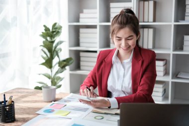 Güzel Asyalı iş kadını dizüstü bilgisayar üzerinde çalışıyor ve istatistik veri grafikleri ve grafiklerinden finansal hesap makinesi ile hesap yapıyor. Modern ofiste başarılı iş sonuçları kırmızı gömlek giyer. Yüksek kalite