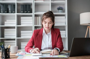 Güzel Asyalı iş kadını dizüstü bilgisayar üzerinde çalışıyor ve istatistik veri grafikleri ve grafiklerinden finansal hesap makinesi ile hesap yapıyor. Modern ofiste başarılı iş sonuçları kırmızı gömlek giyer. Yüksek kalite