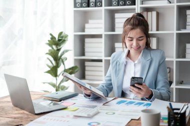 Güzel Asyalı iş kadını dizüstü bilgisayar üzerinde çalışıyor ve istatistik veri grafikleri ve grafiklerinden finansal hesap makinesi ile hesap yapıyor. Modern ofiste başarılı iş sonuçları mavi gömlek giyer. Yüksek