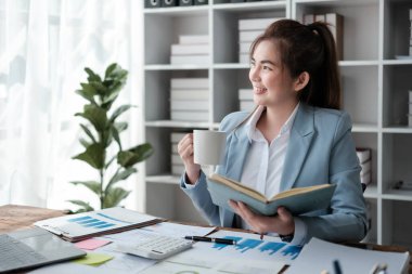 Güzel Asyalı iş kadını dizüstü bilgisayar üzerinde çalışıyor ve istatistik veri grafikleri ve grafiklerinden finansal hesap makinesi ile hesap yapıyor. Modern ofiste başarılı iş sonuçları mavi gömlek giyer. Yüksek