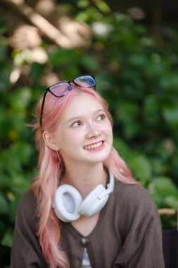 Şirin pembe saçlı bir kız dijital tablete resim çiziyor ve bahçede kulaklık takıyor, Bahçede Serbest Çalışan bir kadın ve dijital tabletli bir kadın. Yüksek Kalite Fotoğraf.
