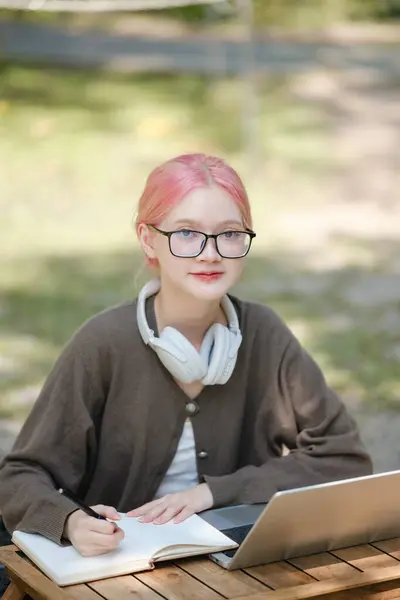 Young woman with a laptop and notes studying in the park for education in nature to relax and learn online. High-quality photo