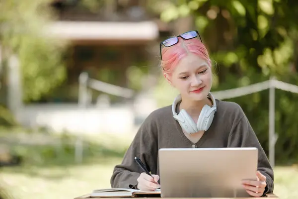 Young woman with a laptop and notes studying in the park for education in nature to relax and learn online. High-quality photo