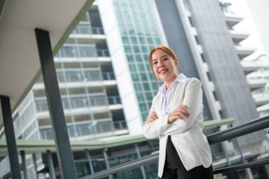 Asyalı mutlu bir iş kadınının portresi. Kollarını kavuşturup ofisinin yanında duran kameraya bakıyor. Büyük bir bina altyapısı var. Yüksek kaliteli fotoğraf..