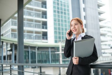 Takım elbiseli genç bir Asyalı iş kadını büyük bir şehirdeki ofise doğru yürüyordu. Genç Asyalı iş kadınları müşterileriyle iletişim kurmak için akıllı telefon kullanıyor. Yüksek Kalite Fotoğraf.