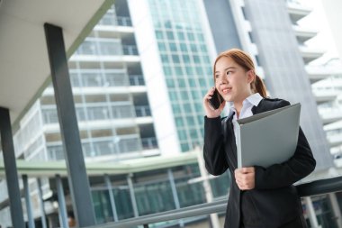 Takım elbiseli genç bir Asyalı iş kadını büyük bir şehirdeki ofise doğru yürüyordu. Genç Asyalı iş kadınları müşterileriyle iletişim kurmak için akıllı telefon kullanıyor. Yüksek Kalite Fotoğraf.