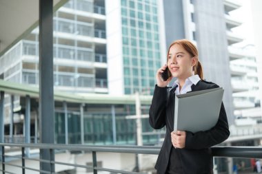 Takım elbiseli genç bir Asyalı iş kadını büyük bir şehirdeki ofise doğru yürüyordu. Genç Asyalı iş kadınları müşterileriyle iletişim kurmak için akıllı telefon kullanıyor. Yüksek Kalite Fotoğraf.