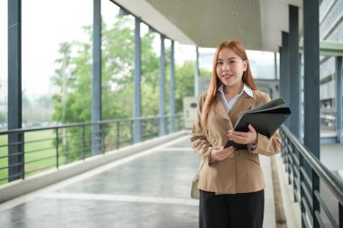 Takım elbiseli genç bir Asyalı iş kadını şehir merkezindeki kalabalık bir şehirde dosyaları tutuyor. Genç Asyalı iş kadınları müşterileriyle iletişim kurmak için akıllı telefon mesajları kullanıyor. Yüksek Kalite Fotoğraf.