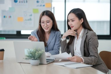 İki kadın bir dizüstü bilgisayar ve bir yığın kağıtla bir masada oturuyorlar. Önemli bir şeyi tartışıyorlar, muhtemelen işle ya da bir projeyle ilgili. Atmosfer ciddi ve odaklanmış görünüyor.