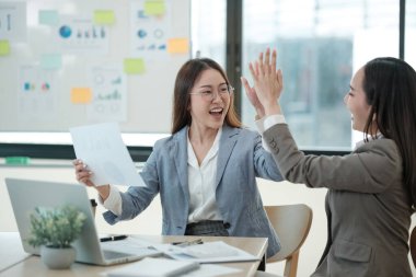 İş ortamında iki kadın birbirine beşlik çakıyor. İçlerinden biri bir kağıt parçası tutuyor.