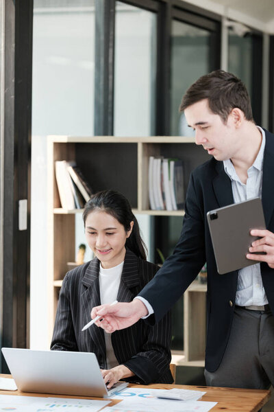 A man and a woman are standing in front of a desk with a laptop and a tablet