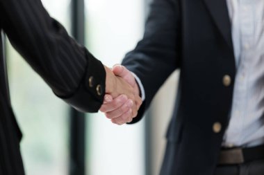 İş ortamında tokalaşan iki kişi. Sağdaki adam takım elbise giyiyor ve kadın da ceket ve kravat takıyor.