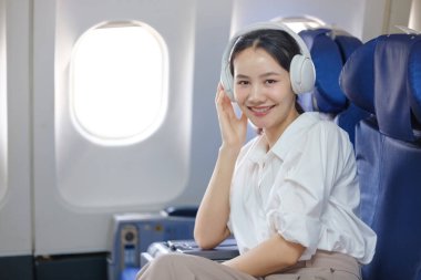 Uçakta kulaklıklı bir kadın oturuyor. Gülümsüyor ve müziğin tadını çıkarıyor.