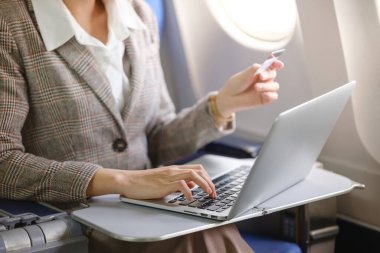 Bir kadın uçakta dizüstü bilgisayarı açık ve elinde kredi kartıyla oturuyor. Uçuşunda muhtemelen çalışıyor ya da internette geziniyor.