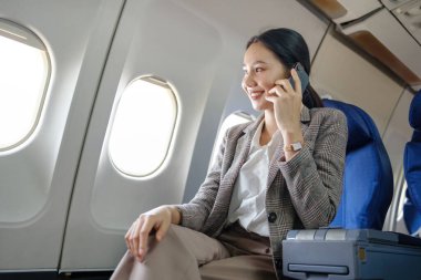 Bir kadın uçakta oturuyor ve cep telefonuyla konuşuyor. Gülümsüyor ve sohbetten zevk alıyor.