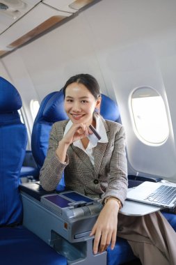 Önünde dizüstü bilgisayarı açık bir kadın uçakta oturuyor. Gülümsüyor ve uçuşun tadını çıkarıyor.
