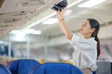 Uçakta bir kadın şapkaya uzanıyor. Sahne neşeli ve şen şakrak, kadın şapkasını üst kompartımandan çıkarmaya çalışıyor.