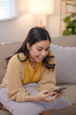 Bir kadın kanepede oturuyor ve cep telefonuna bakıyor. Gülümsüyor ve eğleniyor.