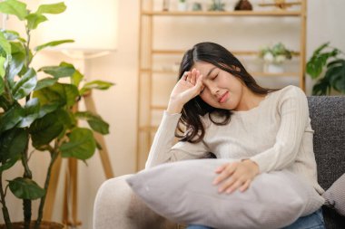 Kucağında yastıkla kanepede oturan bir kadın. Aşağıya bakıyor ve acı çekiyor.