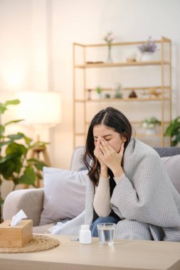 Yanında mendil kutusu olan bir kadın kanepede oturuyor. Burnunu tutuyor ve acı çekiyor.