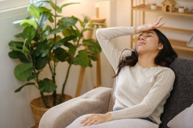 Eli alnında bir sandalyede oturan bir kadın. Yorgun görünüyor ve terliyor.