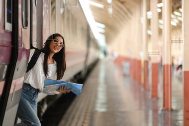 Bir kadın elinde haritayla tren peronunda duruyor. Gülümsüyor ve yaklaşan yolculuğu için heyecanlı.