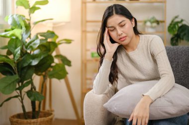 Bir kadın kafasının arkasında yastıkla kanepede oturuyor. Aşağıya bakıyor ve acı çekiyor.