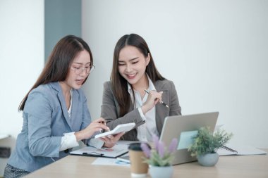 İki kadın bir dizüstü bilgisayar ve hesap makinesiyle bir masada oturuyor. Birlikte bir proje üzerinde çalışıyorlar.