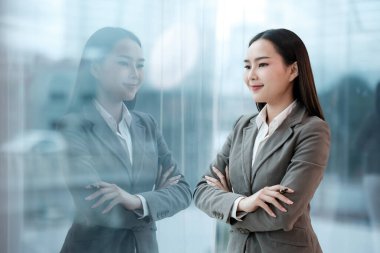 Takım elbiseli bir kadın bir pencerenin önünde duruyor, sokağa bakıyor. Siyah bir yüzük ve gümüş bir bilezik takıyor.