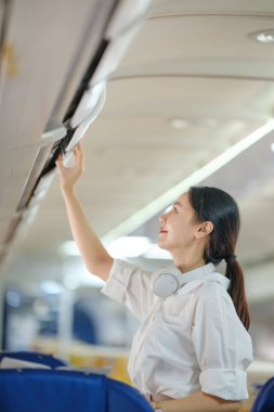 Bir kadın bir uçağın havalandırmasını temizliyor. Gülümsüyor ve işinden zevk alıyor.