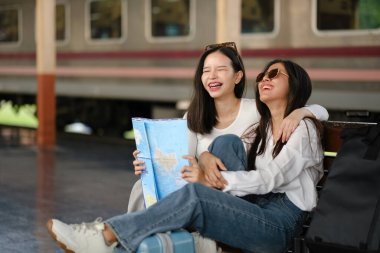 Elinde haritayla bankta oturan iki kadın. Gülüyorlar ve gülüyorlar. Bir tanesi güneş gözlüğü takıyor.